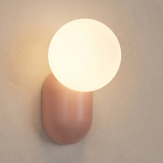 Luma glass globe wall sconce light, rose pink back, studio shot on a neutral backdrop