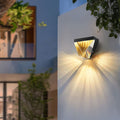 Diamond outdoor wall light in black glowing among plants at dusk