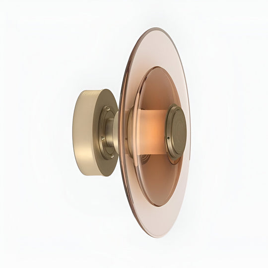 Nordic glass disc wall sconce light, amber-peach pane on a brass mount, angled view