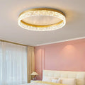 Modern round ceiling light, gold rim above a bed by a pink wall