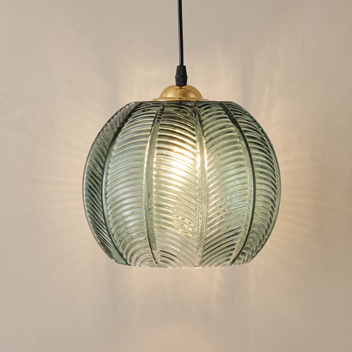 Leaf pattern glass globe pendant light in green with a brass cap, studio shot on a neutral backdrop
