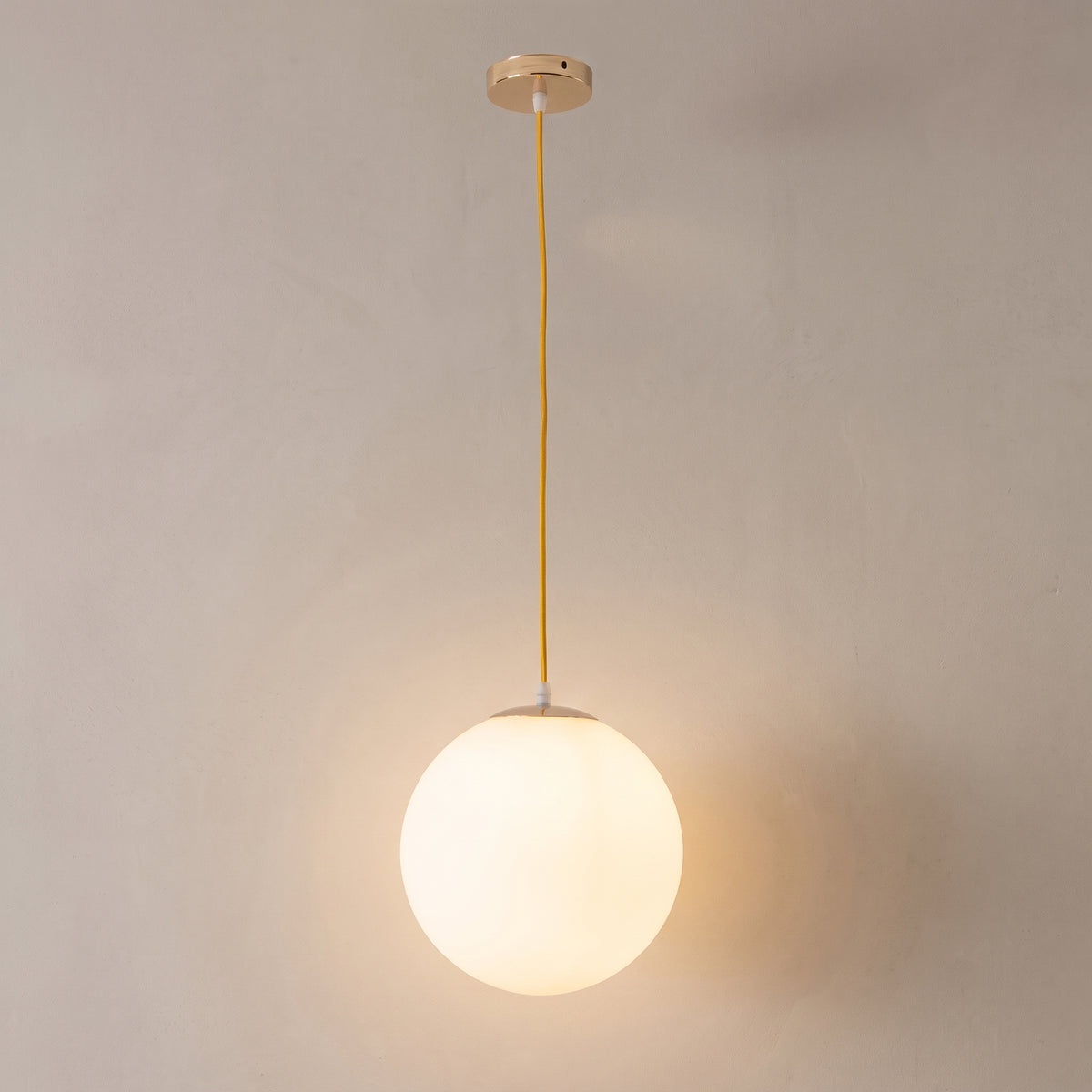 Nordic milk glass globe pendant light, gold cable and canopy, studio shot on a neutral backdrop